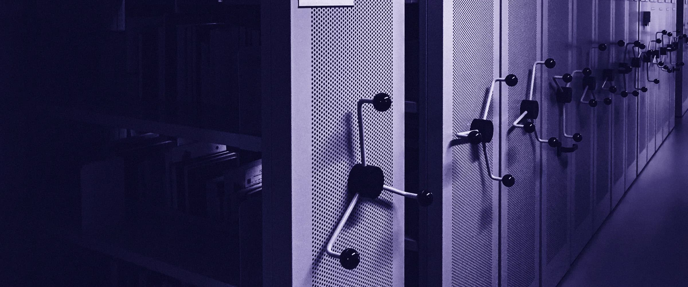 A records room of mobile archive shelving, the units rolled together with their crank handles in a row and one aisle of files open on the left.
