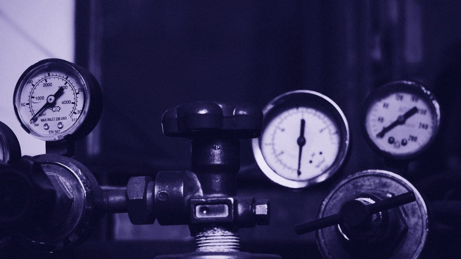 Pressure gauges and a valve handle on a gas cylinder regulator, seen close up.